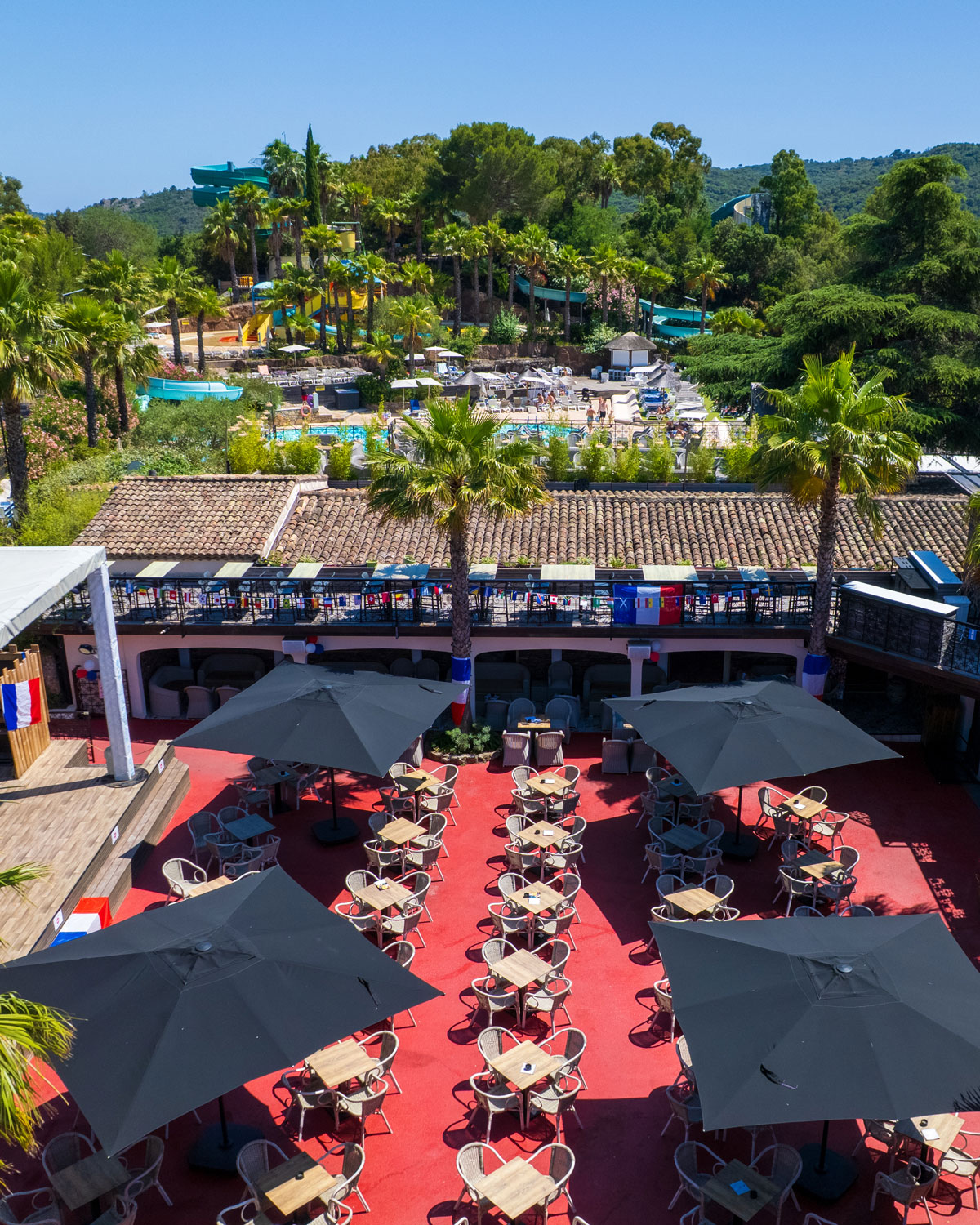 Bar terrace at Esterel Caravaning under its parasols, with palm trees and the water park slides in the background